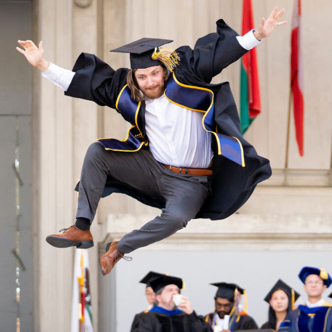 A graduate mid-jump on stage during the Baccalaureate ceremony.