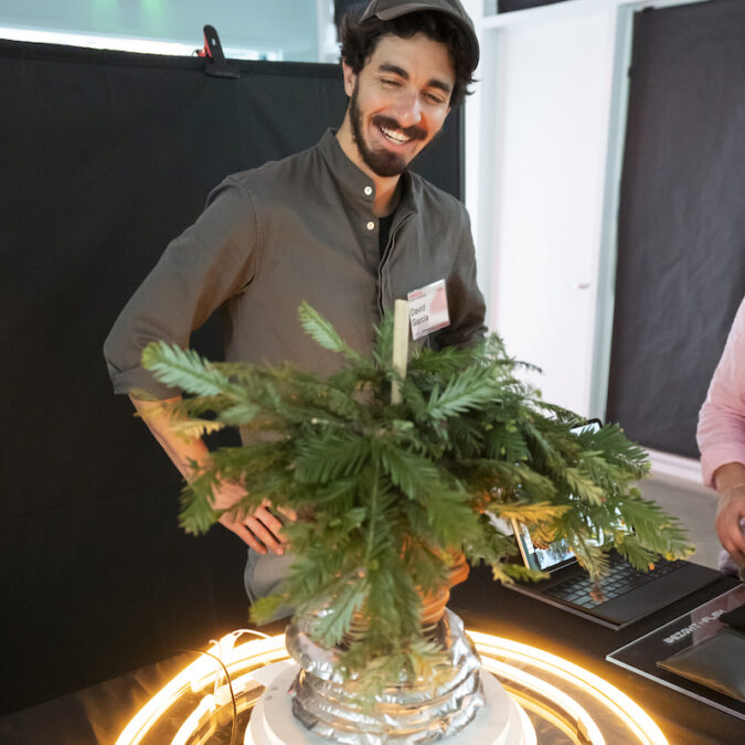 A student smiles at a class project involving a plant surrounded by light.