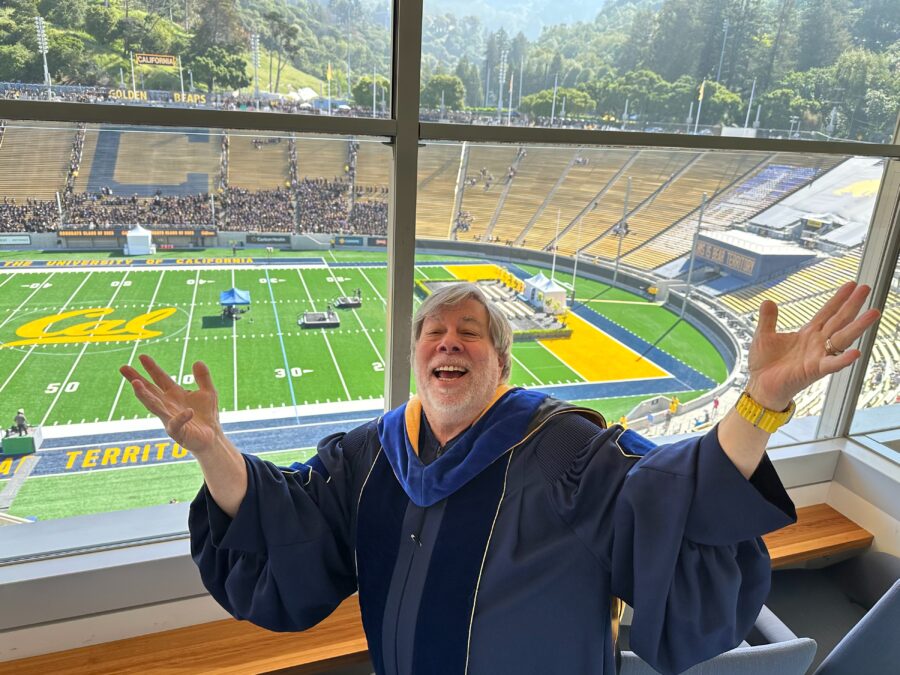 Steve Wozniak in graduation regalia, posing with arms wide open in front of California Memorial Stadium.