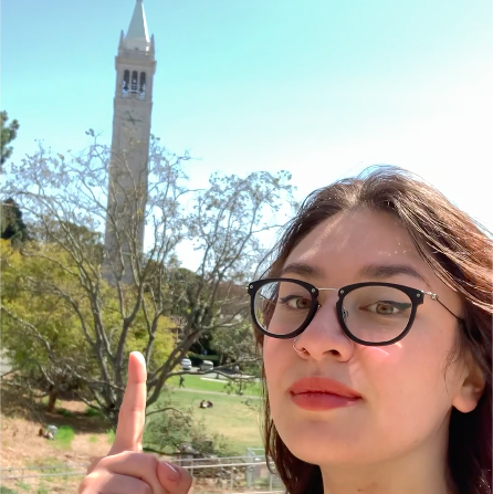 A selfie of a Romy Mastel pointing up at the Campanile in the distance.