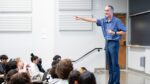 Dan Garcia lectures in front of a classroom with seated students in front of him. Several students have their hands raised.