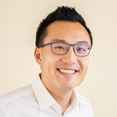 Headshot of Tony Xu in a white shirt in front of a tan background